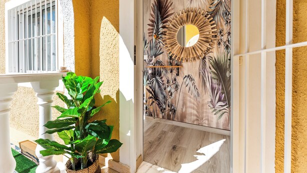 A room with a wooden floor, a large mirror with a sunburst frame, and a tropical leaf pattern on the wall. - Sun-Kissed 3BR Townhouse by Pool, Near Carabassi Beach (Gran Alacant)