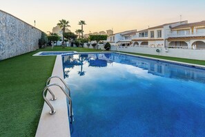 Ein Swimmingpool mit einer Steinwand, umgeben von gepflegtem Rasen und Palmen.
