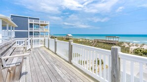 A wooden deck with a white railing overlooking a beach and a building with multiple balconies. - 2nd Wind - 2nd Row 3 BR Home - 2nd Floor Observation Deck (Surf City)