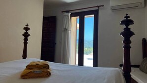 Ett hotellrum med en säng, ett fönster med gardiner, en luftkonditioneringsanläggning och utsikt över omgivningarna.
