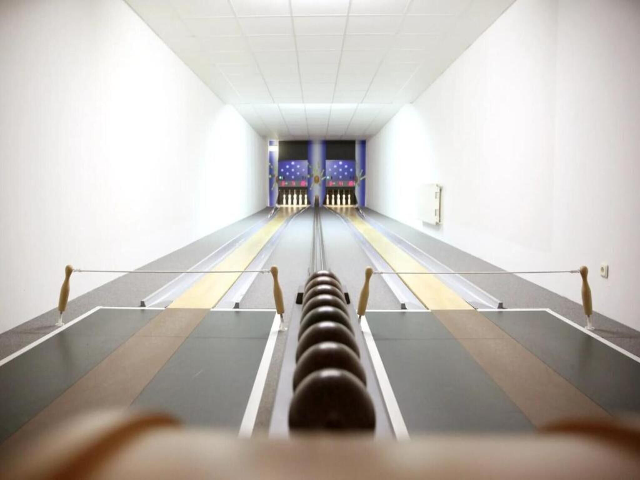 A bowling alley with lanes, pins, and a bowling ball rack.