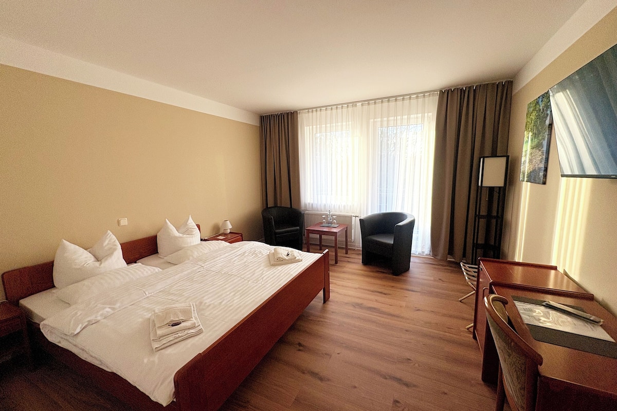 A hotel room with a large bed, a desk, a chair, and a small table.
