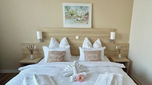 A neatly made bed with white linens, two pillows with 'happy place' text, and a painting above the headboard. - Kaiserhof Feldberg by Belvilla Resorts (Feldberger Seenlandschaft)