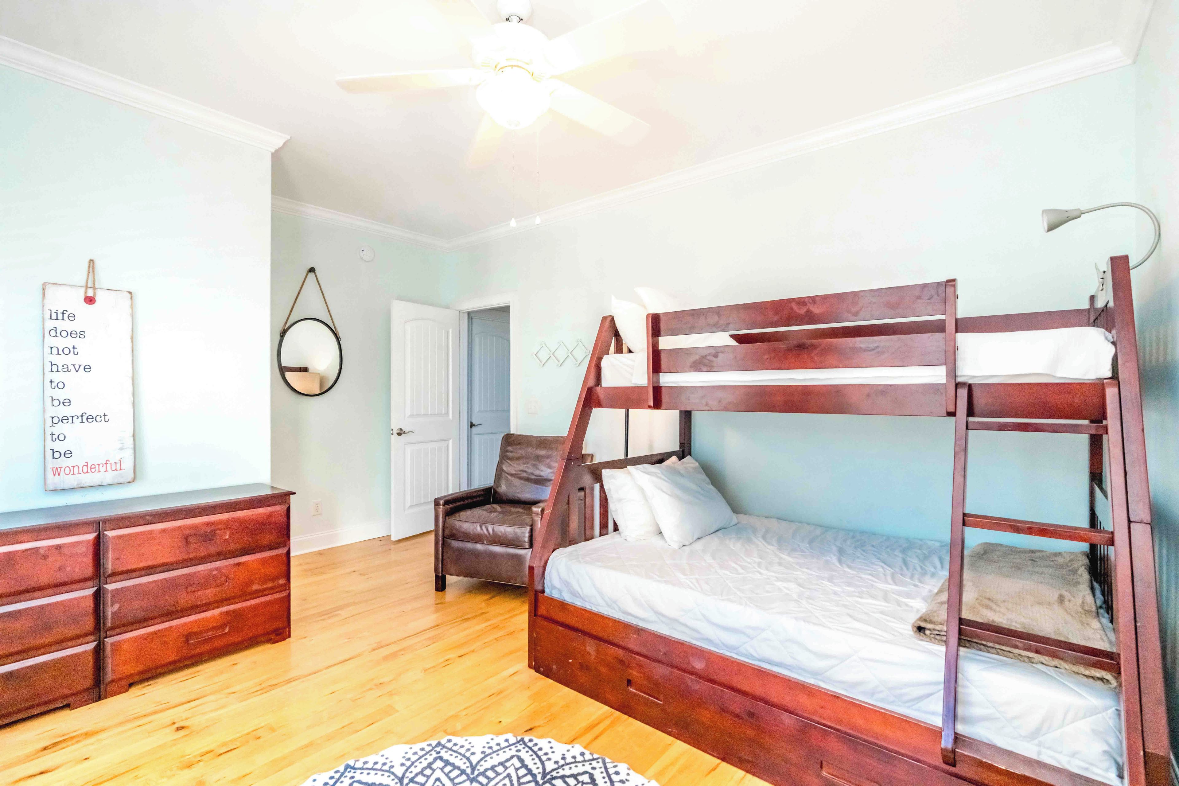 A bedroom with a bunk bed, a dresser, a chair, a mirror, and a wall with a motivational quote.