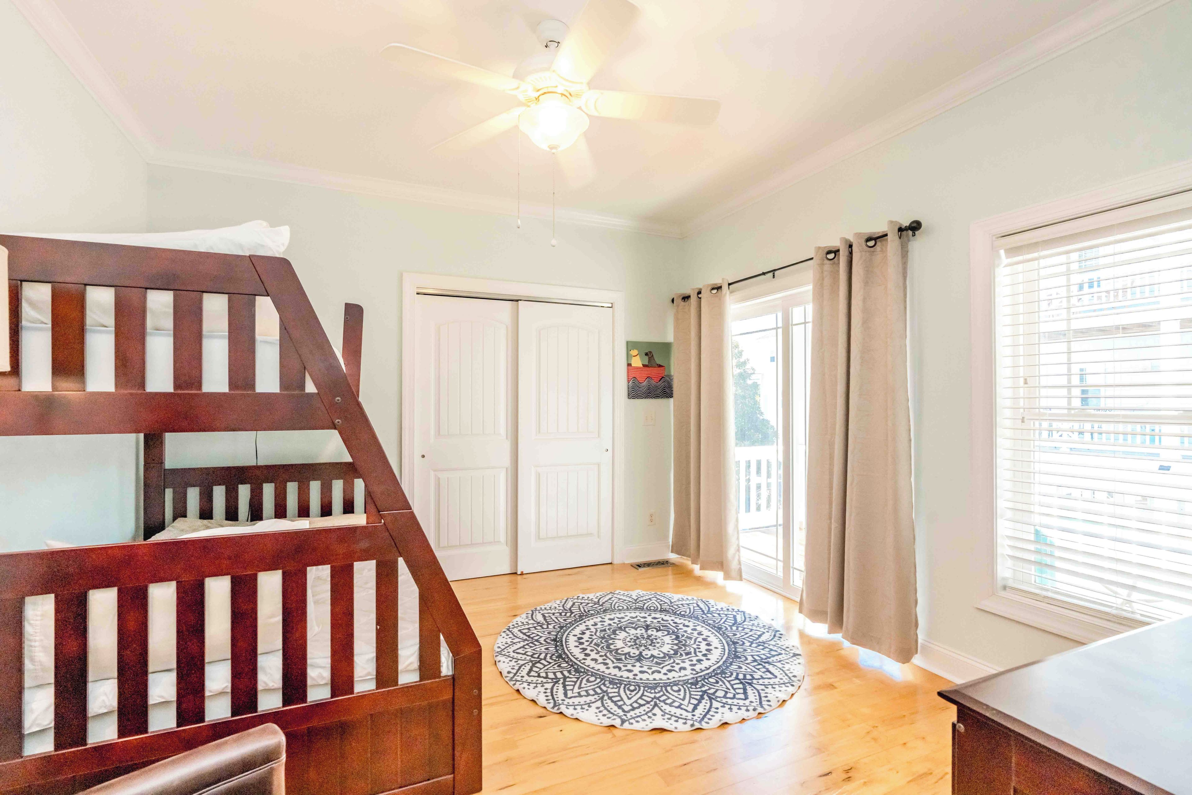 A room with a bunk bed, a ceiling fan, a door, and a window with curtains.