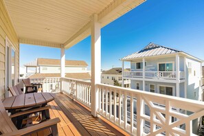 A covered outdoor deck with a table and chairs, overlooking a residential area with houses. - Soundside Sunsets - Gorgeous Home with Gorgeous Sound Views; 4 BR/4.5 Baths (Surf City)