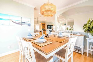 Comedor con mesa de madera dispuesta para cuatro personas, sillas blancas y una lámpara colgante.