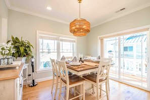 A dining area with a wooden table, white chairs, and a hanging light fixture. - Soundside Sunsets - Gorgeous Home with Gorgeous Sound Views; 4 BR/4.5 Baths (Surf City)