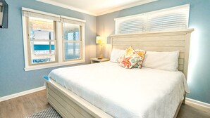 Ein Schlafzimmer mit einem Bett, einem Nachttisch, einer Lampe, einem Deckenventilator und einem Fenster mit Jalousien.