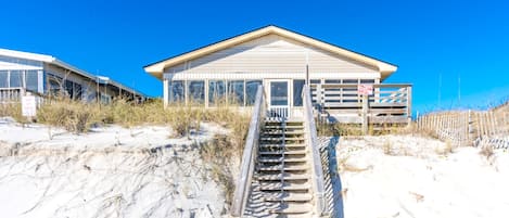 A beach house with a staircase leading to a wooden deck.
