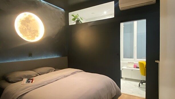Um quarto moderno com uma cama, uma luminária fixada na parede e uma janela.