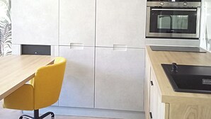 Cozinha moderna com mesa de jantar de madeira, uma cadeira amarela, forno embutido e luminária.