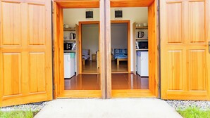 A wooden double door leading into a room with a bed, a small table, and a shelf with kitchen items. - Vlaštovčí recreation area (Radvanec)