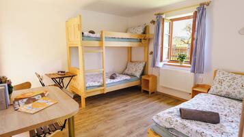 Una habitación con literas, una mesa de madera, una ventana con cortinas y un radiador.