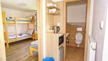 A compact room with bunk beds, a small kitchenette, a toilet, and a blue trash bin.