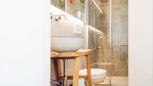 Une salle de bain moderne avec un grand lavabo blanc, un tabouret en bois, des toilettes et une douche séparée par une paroi de verre.