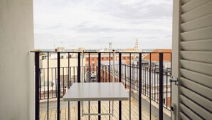 Un balcon avec une table blanche, une rambarde en métal et une vue sur des immeubles et une tour en arrière-plan.