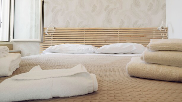 Un lit bien fait, avec du linge de lit blanc et une couvre-lit beige à texture intéressante.