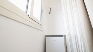 Une pièce avec un mur blanc, une fenêtre avec des stores et un réfrigérateur blanc.