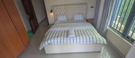 Un dormitorio ordenado con cama, armario y ventana con cortinas.