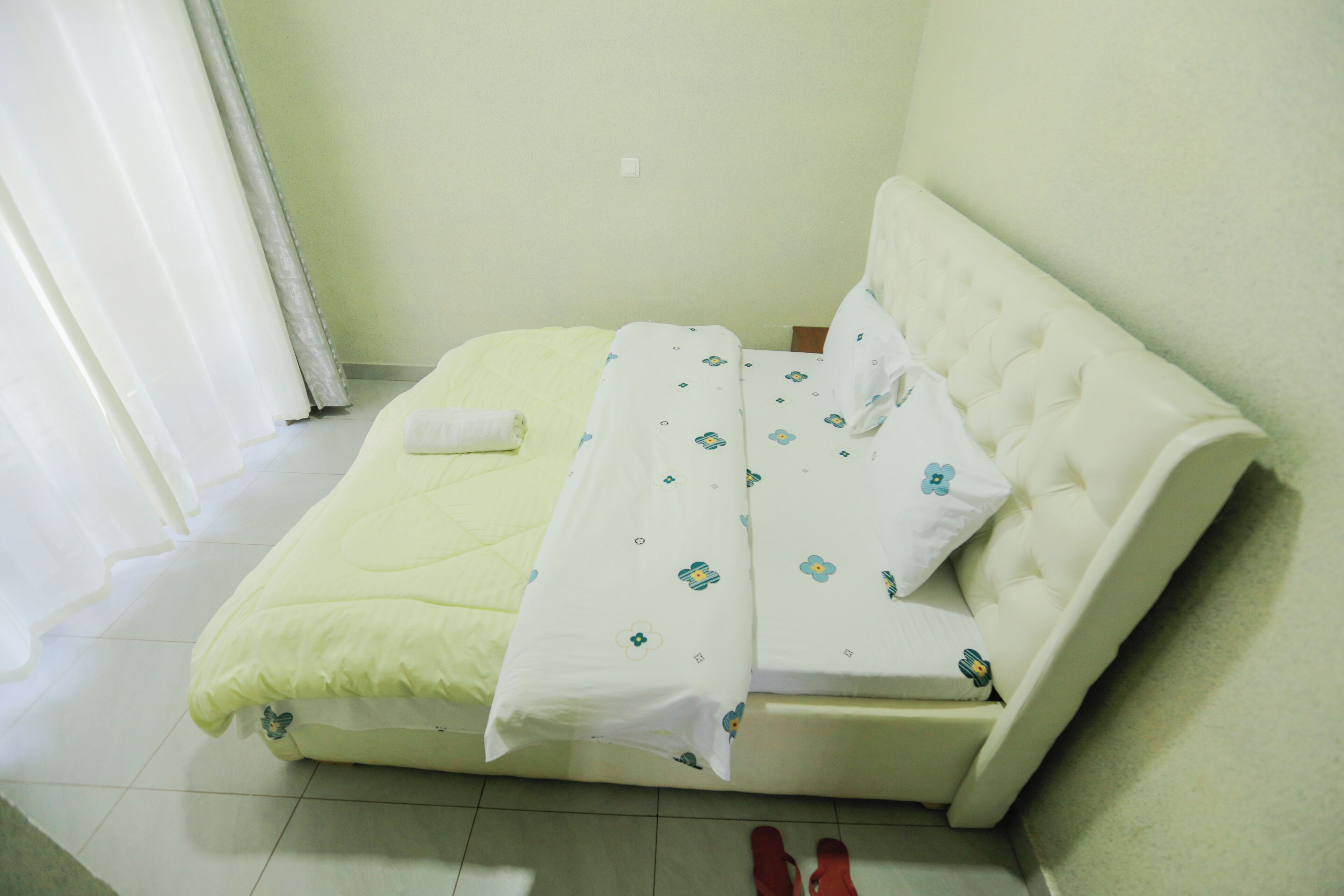 Una cama pequeña y bien hecha, con cabecera blanca y colcha estampada con motivos florales.