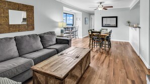 A modern living room with a gray sectional sofa, a wooden coffee table, and a dining area with a wooden table and chairs. - Ocean Dunes Villas (Myrtle Beach)