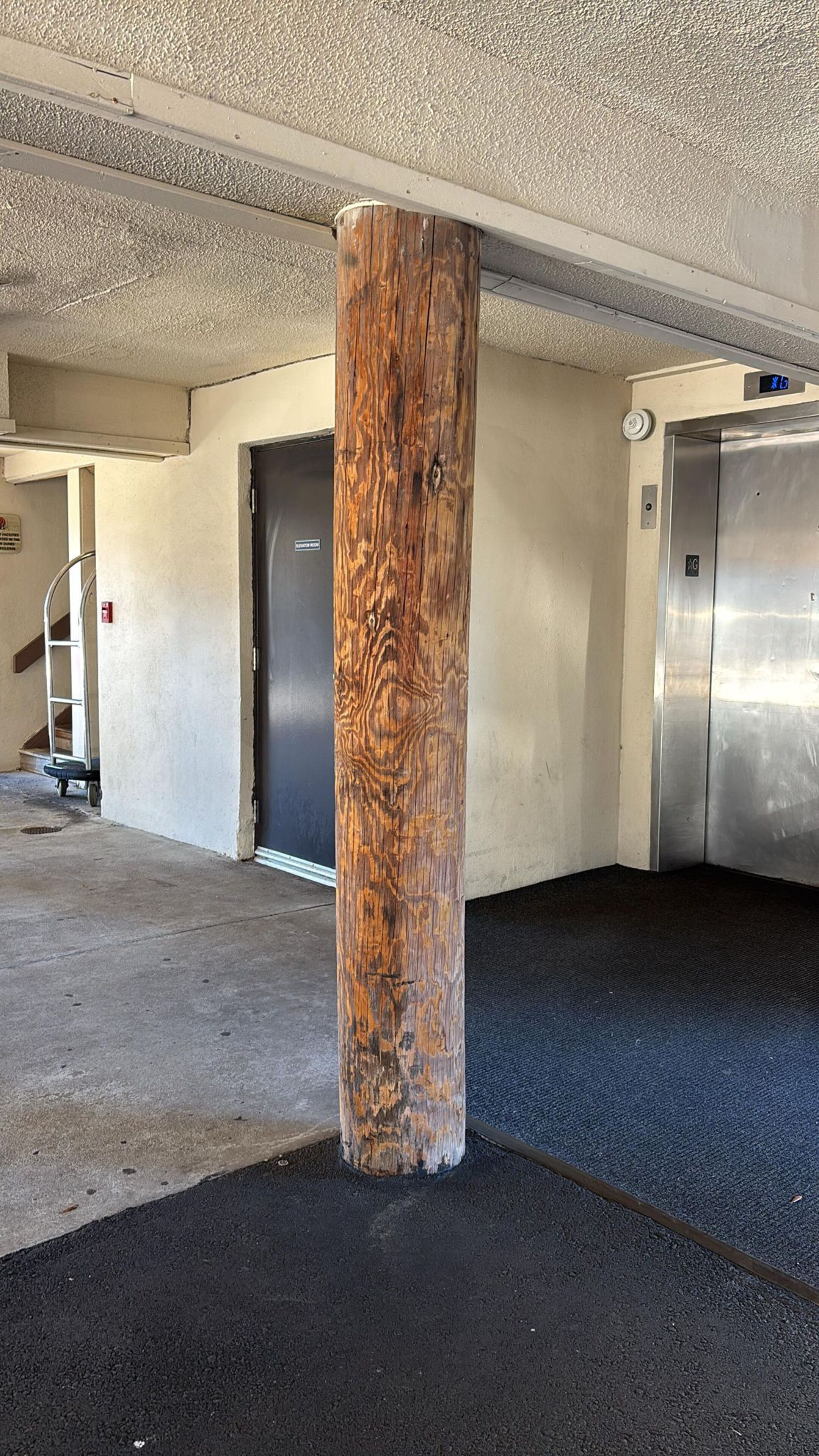 A wooden pillar in a parking garage with a door and an elevator in the background.