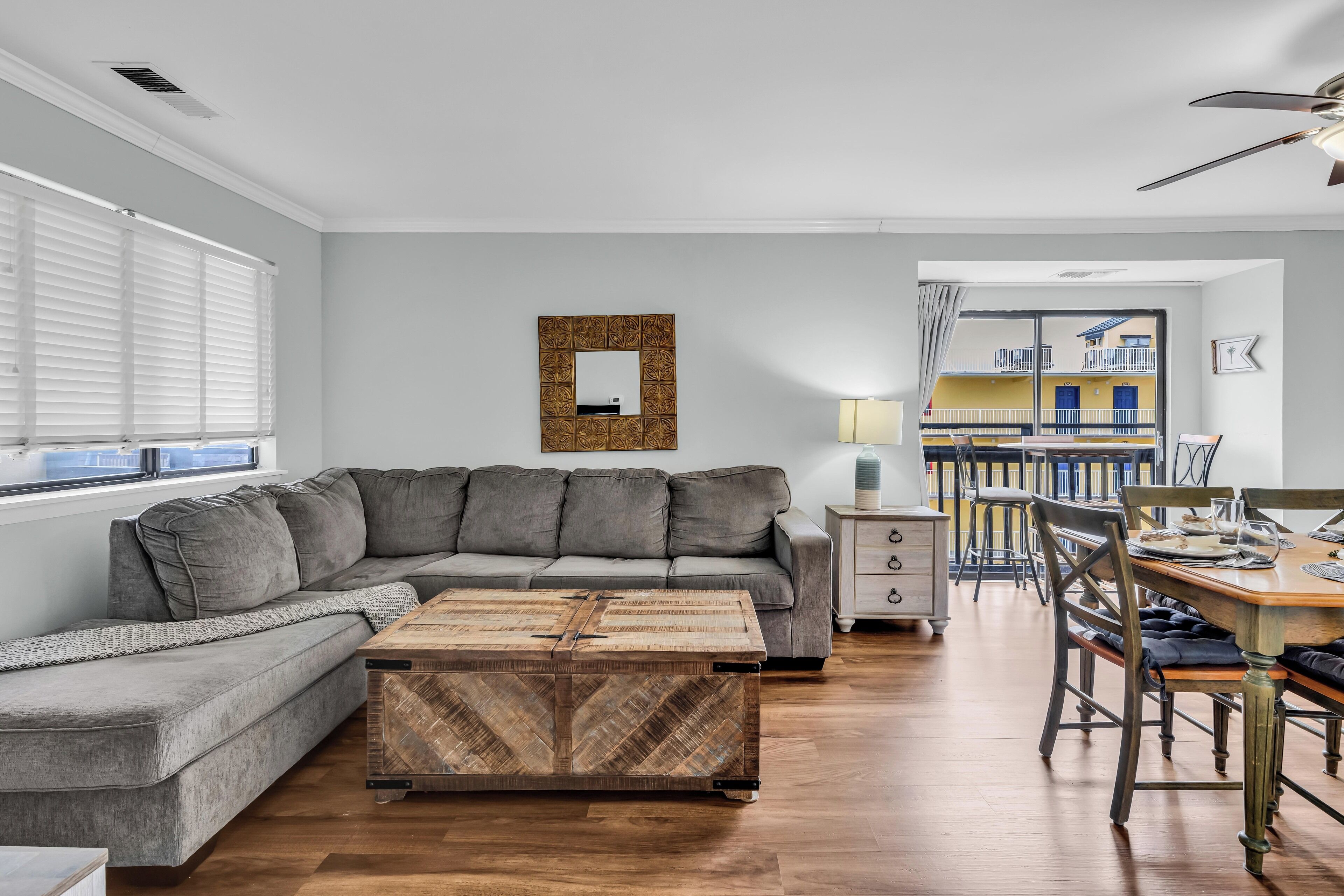 Un salon moderne avec un canapé d’angle, une table basse en bois et un coin repas comprenant une table et des chaises en bois.