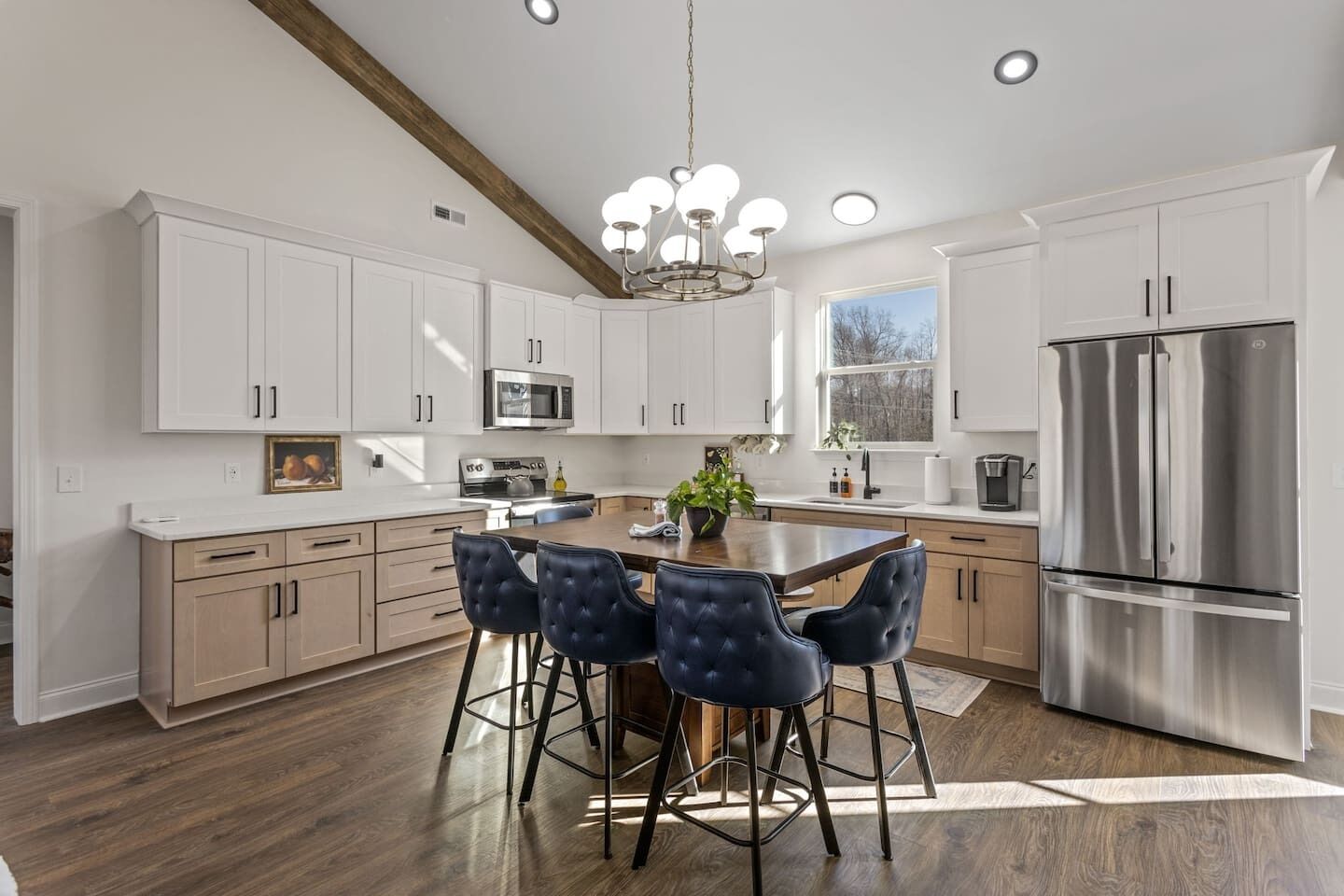 A modern kitchen with white cabinets, a stainless steel refrigerator, a central island with bar stools, and a chandelier.