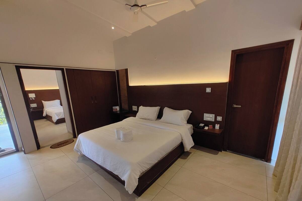 Habitación de hotel con una cama grande, una mesita de noche, un armario y una puerta que da a un balcón.