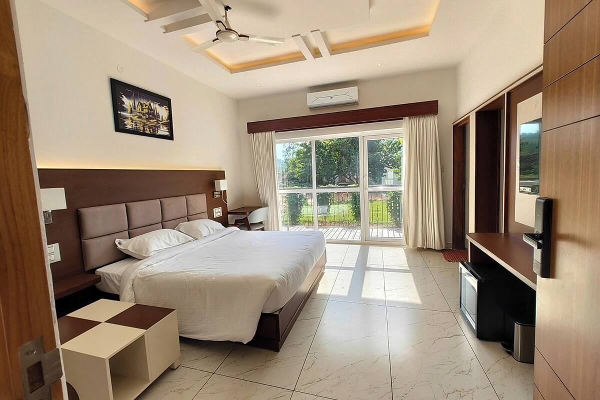 Una habitación de hotel con cama, escritorio, televisor y balcón con cortinas.