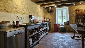 Una cocina rústica con suelo de ladrillo, vigas de madera, un lavamanos y diversos utensilios de cocina.