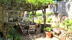 Un espacio de estar al aire libre rústico con un pérgola, una pared de piedra y diversas plantas.