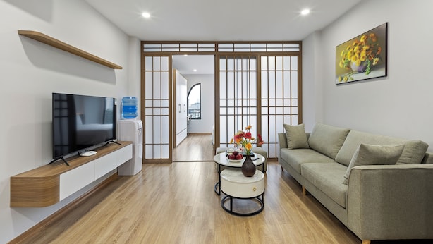 A modern living room with a flat-screen TV, a sofa, a coffee table with a vase, and a water dispenser. - Residence Suite (Hanoi)