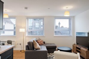 A modern living room with a grey sofa, a small round table, a TV on a wooden stand, and a floor lamp. - City Point Apartments by Guestz (Aberdeen)