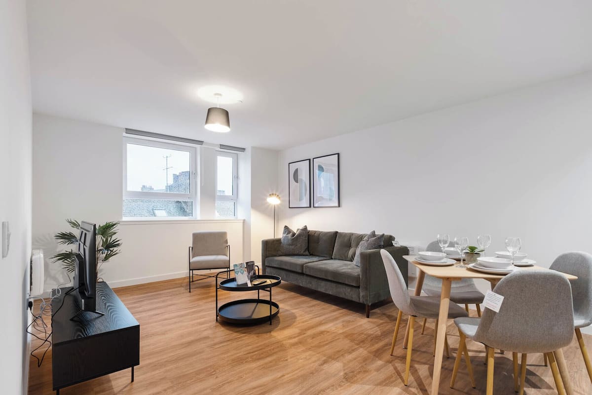 Una sala de estar moderna con un sofá, una mesa de comedor, sillas y un televisor sobre un mueble.