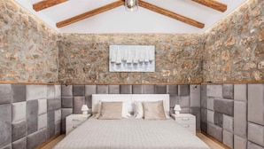 A bedroom with a stone wall, a white headboard, and a bed with a grey upholstered headboard. - Private Stone Villa with heated pool, Near Opatija (Ičići)