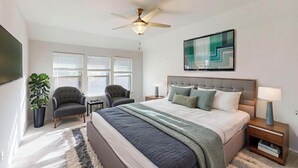 Ein Schlafzimmer mit einem Bett, einem Deckenventilator, einem Fernseher, einem Gemälde und einem Fenster mit Jalousien.