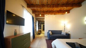 Ein Hotelzimmer mit Flachbildfernseher, Holzboden, einer Couch, einem Bett und einem Schminktisch.