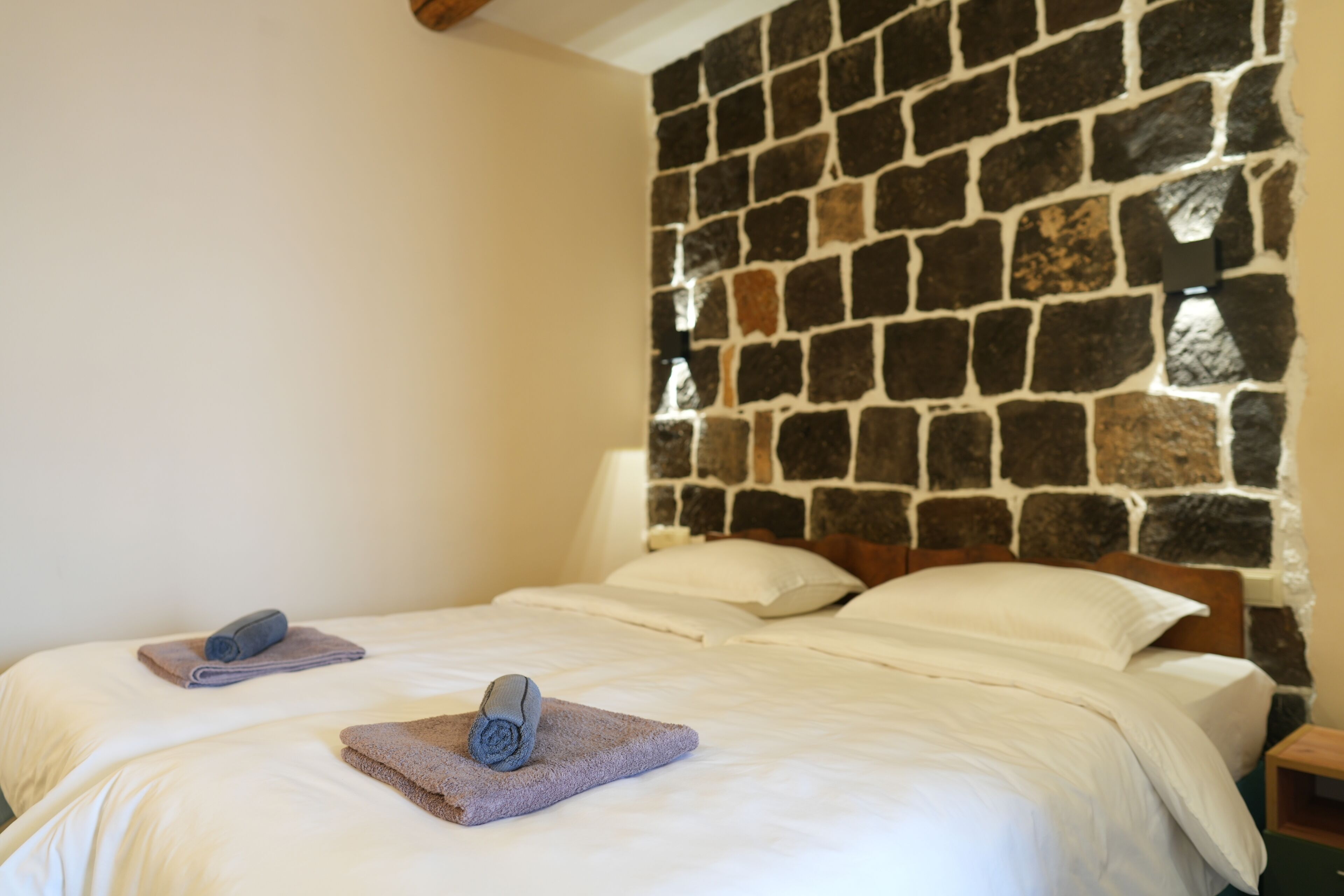 A hotel room with two beds, a stone wall, and a nightstand with a lamp.