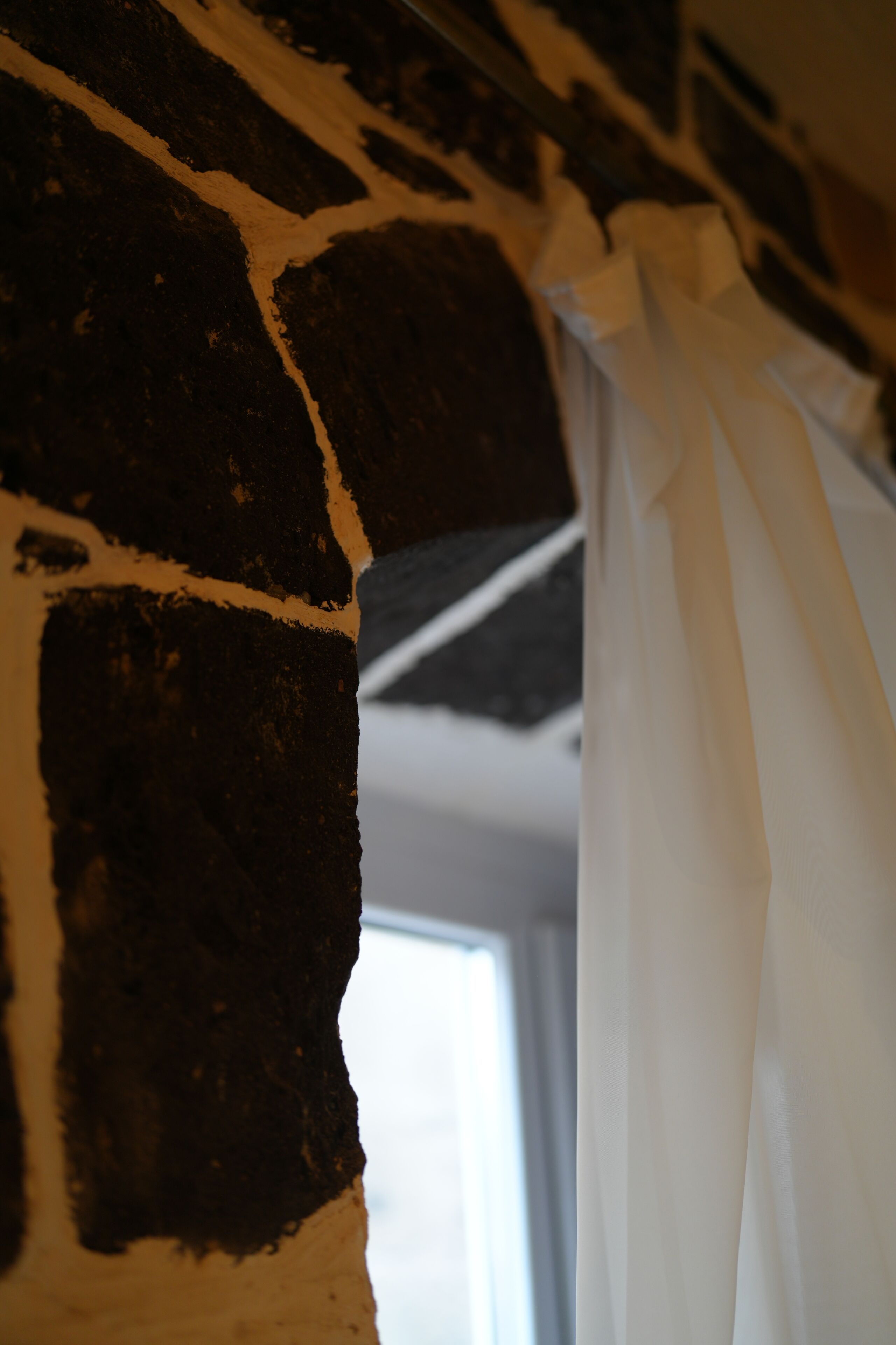 A close-up of a brick wall with a white curtain partially covering a window.