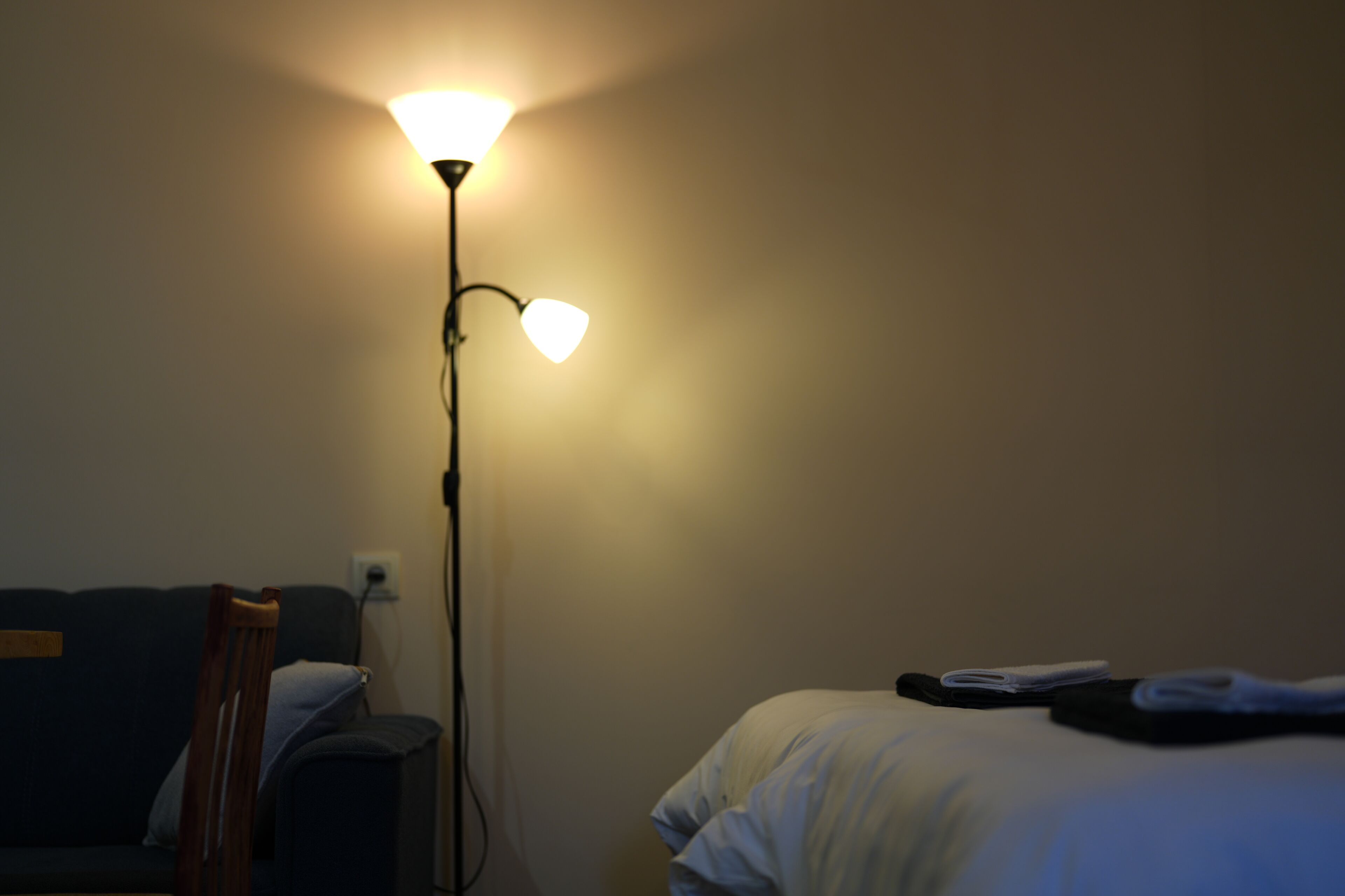 Una stanza scarsamente illuminata con un letto singolo, un comodino e una lampada da terra.