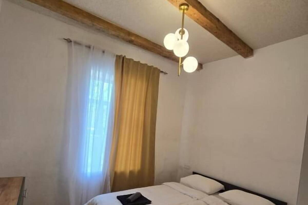 A bedroom with a wooden ceiling, a bed with white linens, a bedside table, and a window with curtains.