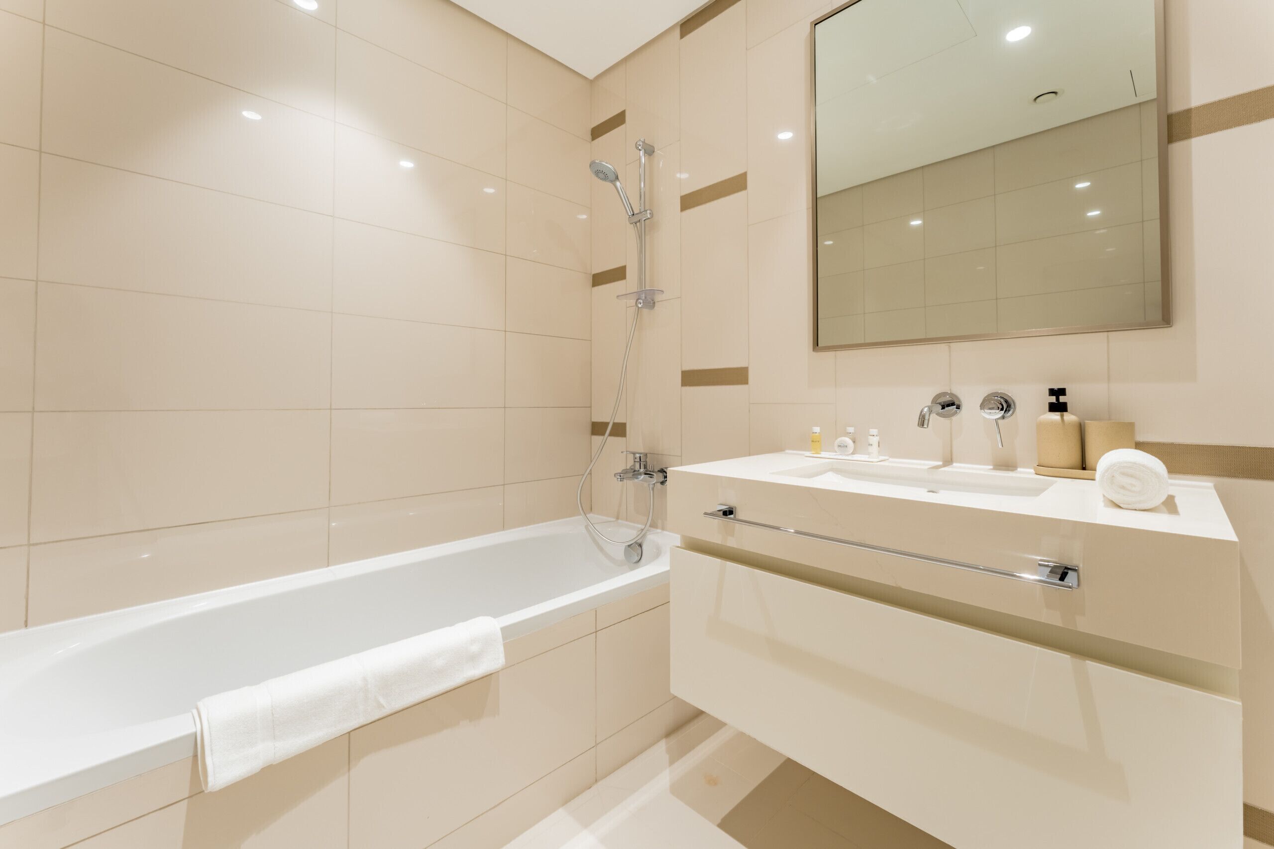 A modern bathroom with a bathtub, a large mirror, and a vanity with a sink and towel rack.
