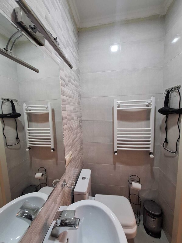 A modern bathroom with two sinks, a toilet, a mirror, and towel racks. - Crystal Hotel Tbilisi (Tbilisi)