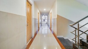 A hotel hallway with a staircase on the right, wooden doors on the left, and a tiled floor. - Sri ganesh Swati residency  (Visakhapatnam)