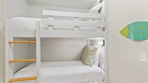 Un lit superposé avec une tête de lit blanche, une échelle en bois et un lit simple en dessous.