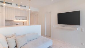 Una sala de estar moderna con un televisor de pantalla plana grande montado en la pared, un sofá de color claro e iluminación colgante.