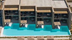 Un hotel de varios pisos con piscinas al aire libre, balcones con mobiliario y fachada de piedra.