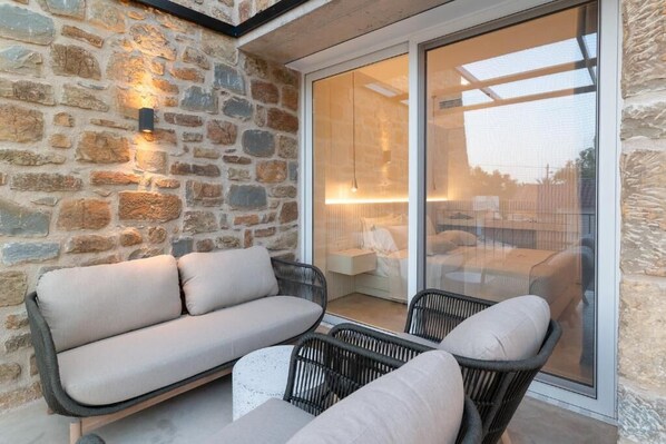 Un mur en pierre, un canapé et des fauteuils, une porte vitrée donnant sur un espace intérieur et une petite table.